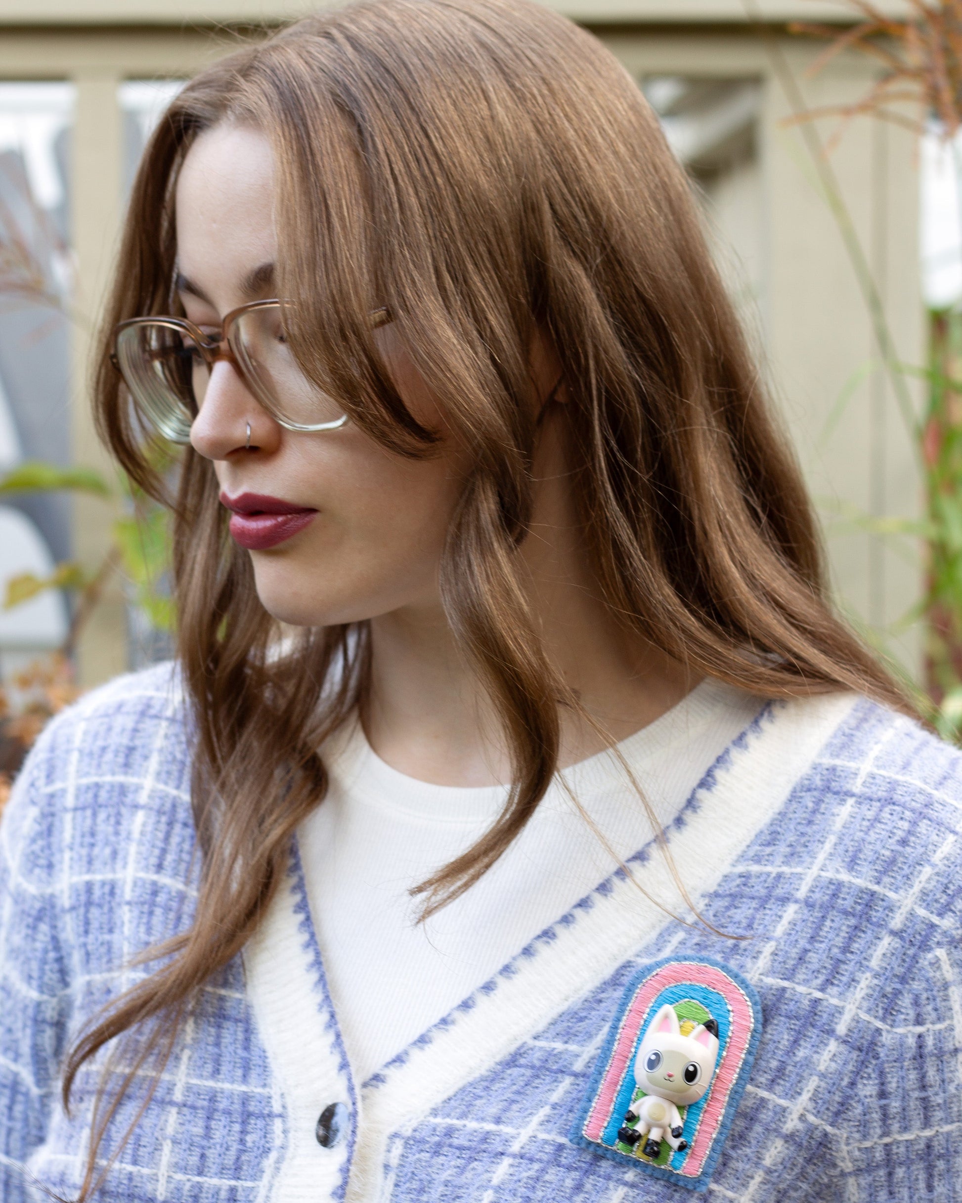 Handmade embroidered rainbow brooch featuring Pandy Paws worn on a blue plaid cardigan by a young woman.