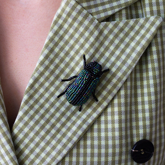Closeup of a green and black handmade beaded beetle brooch worn on a blazer lapel.
