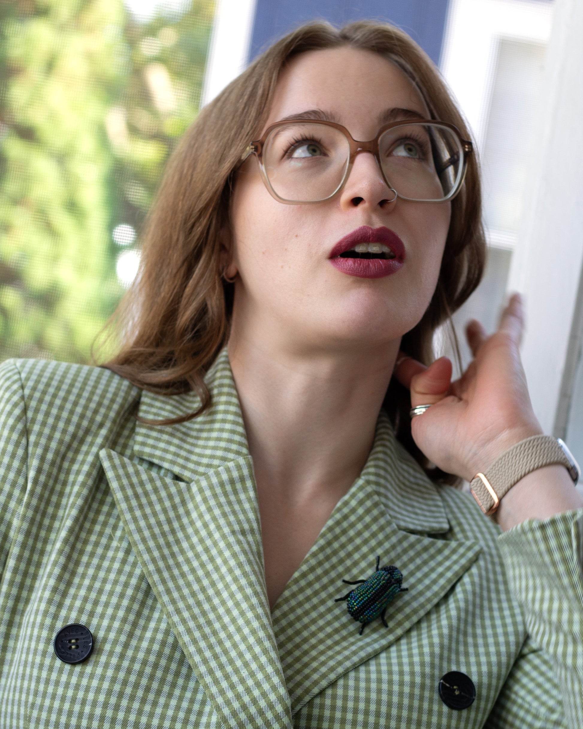 Green and black handmade beaded beetle brooch worn on a blazer lapel by a young woman.