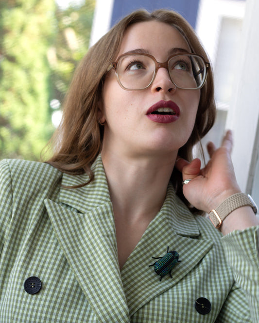 Green and black handmade beaded beetle brooch worn on a blazer lapel by a young woman.