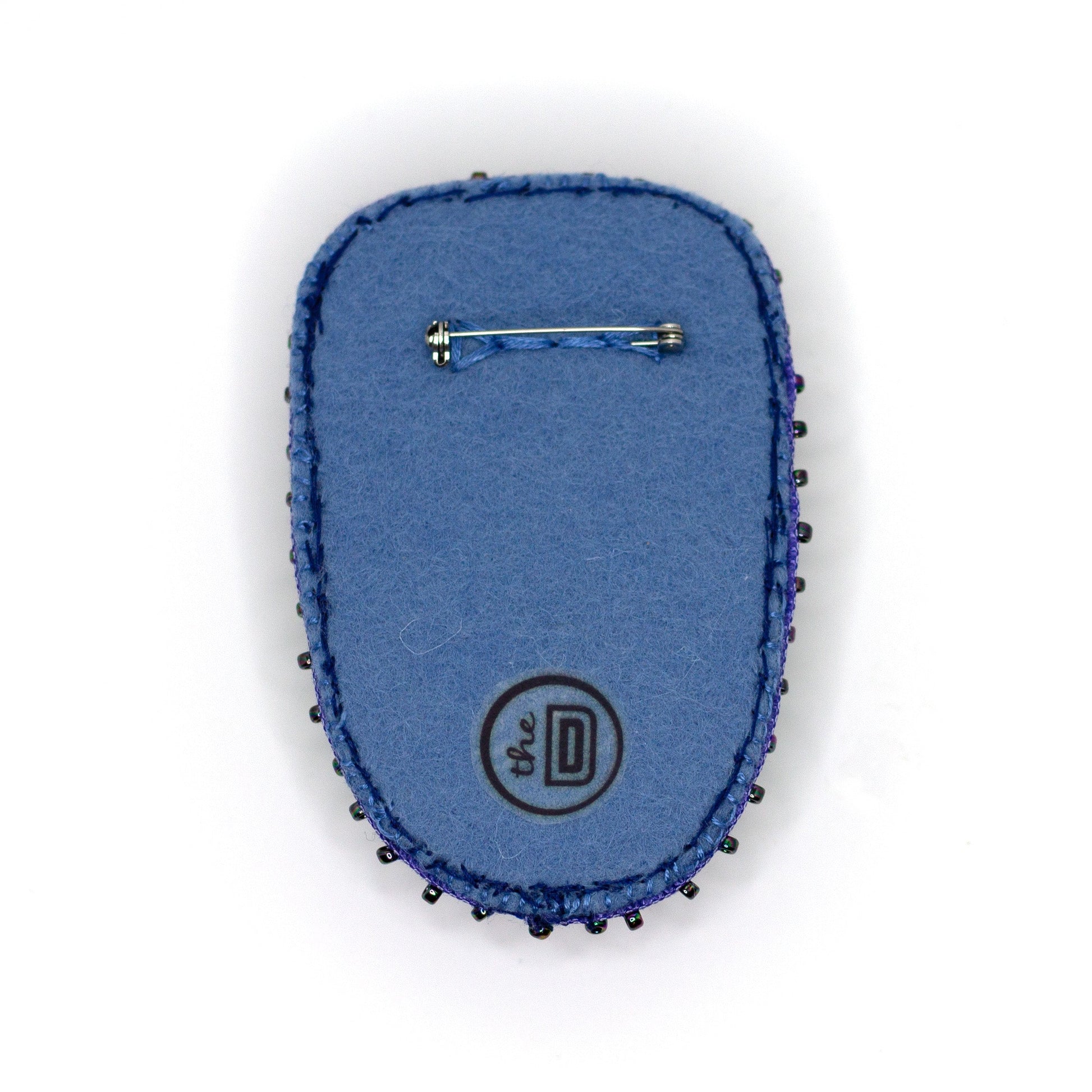 Back view of a handmade sequined brooch featuring a Maleficent doll on a white background showing pin fastener.