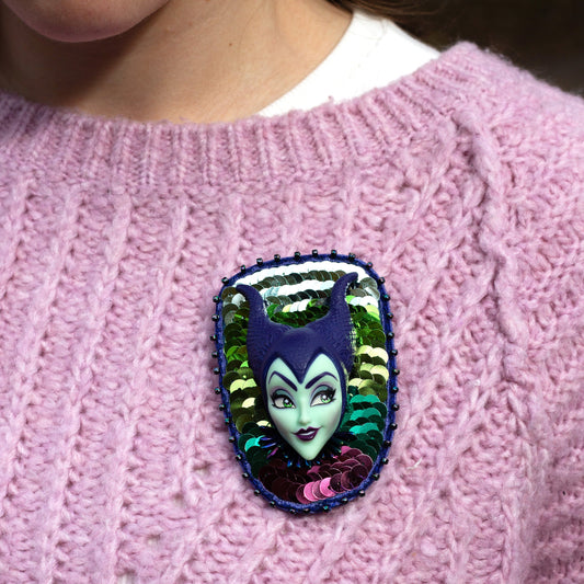Closeup of a handmade purple and green sequined brooch featuring a Maleficent doll worn on a pink sweater.