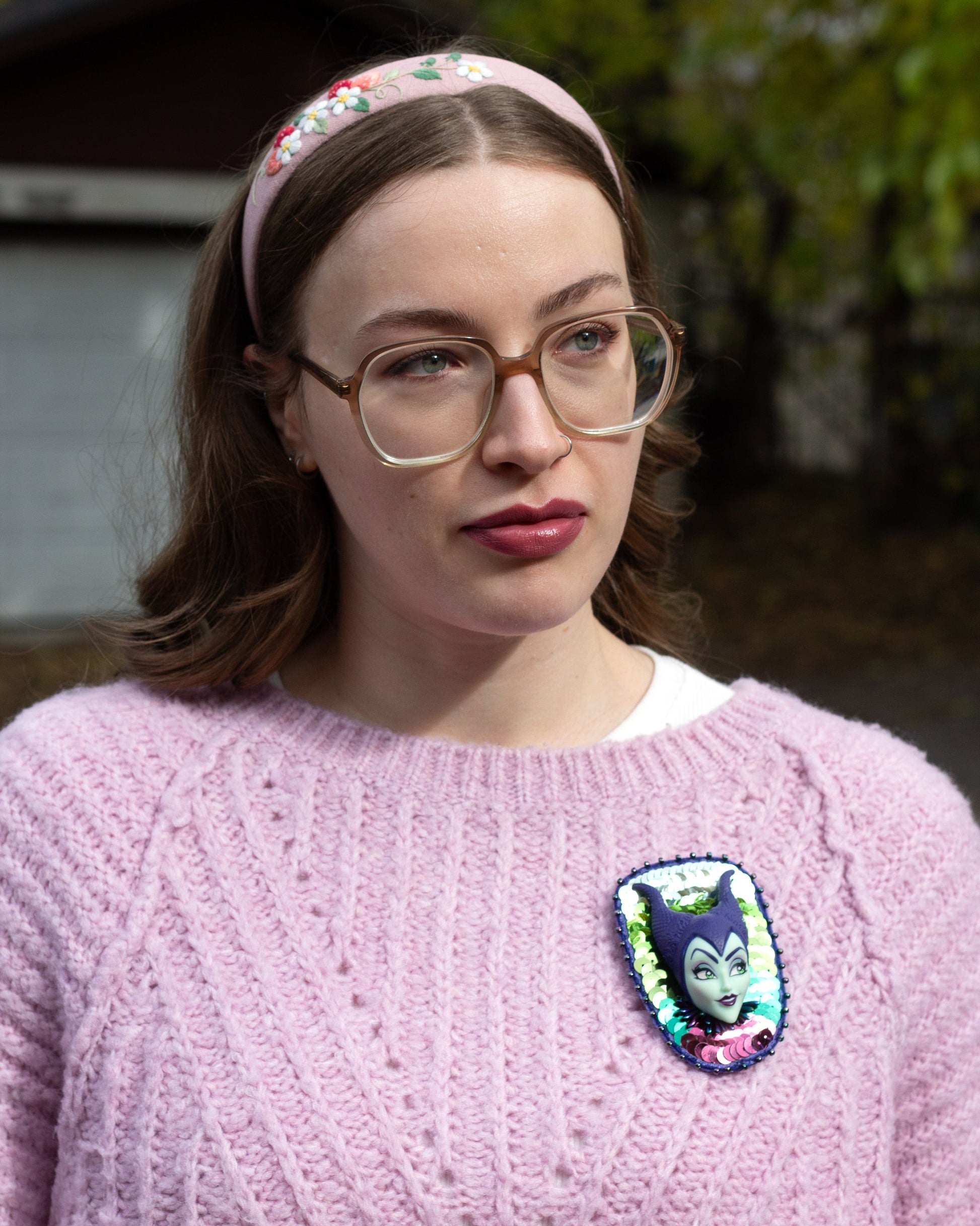 Handmade purple and green sequined brooch featuring a Maleficent doll worn on a pink sweater by a young woman.