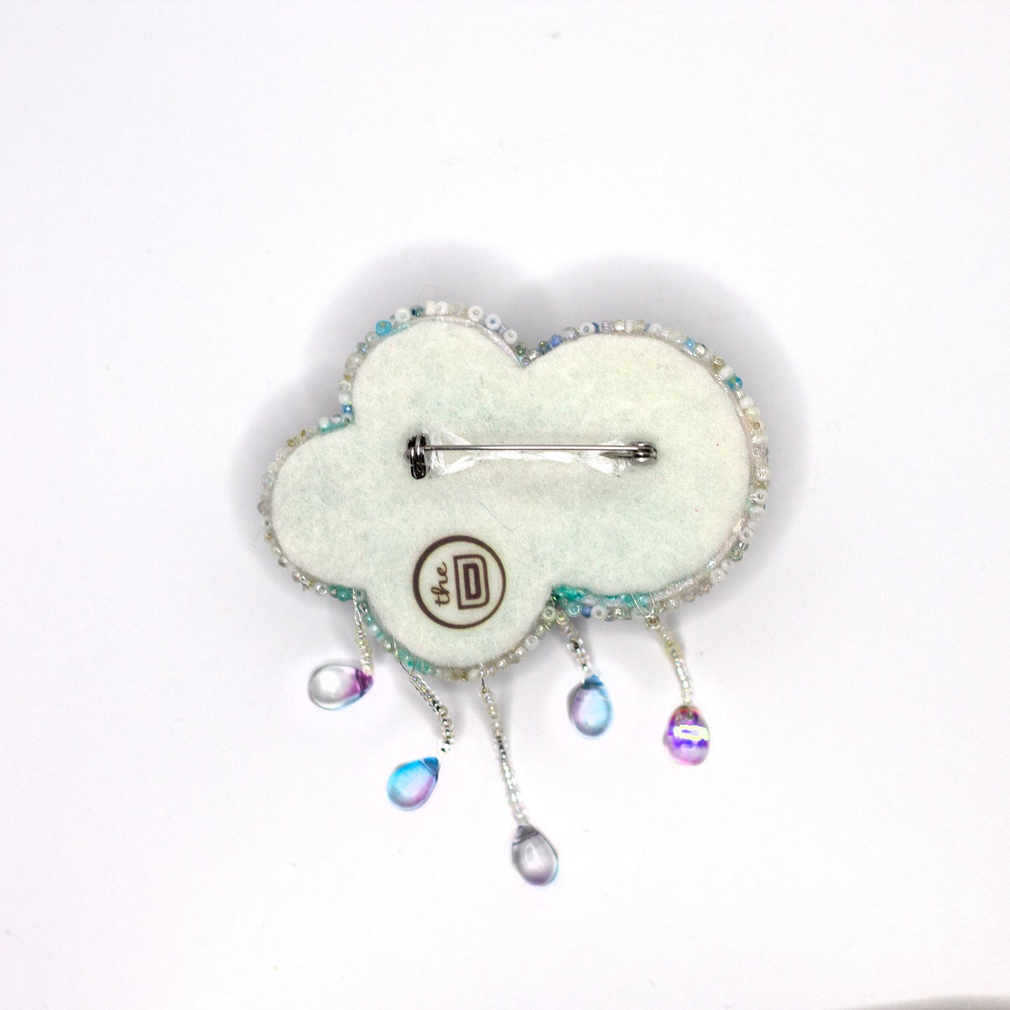 A cloud-shaped beaded brooch with dangling iridescent teardrop charms, shown on a plain white background.