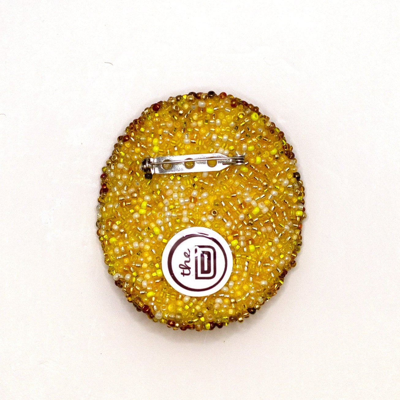 Back view of handmade beaded golden yellow potato chip brooch on a white background showing pin fastener.