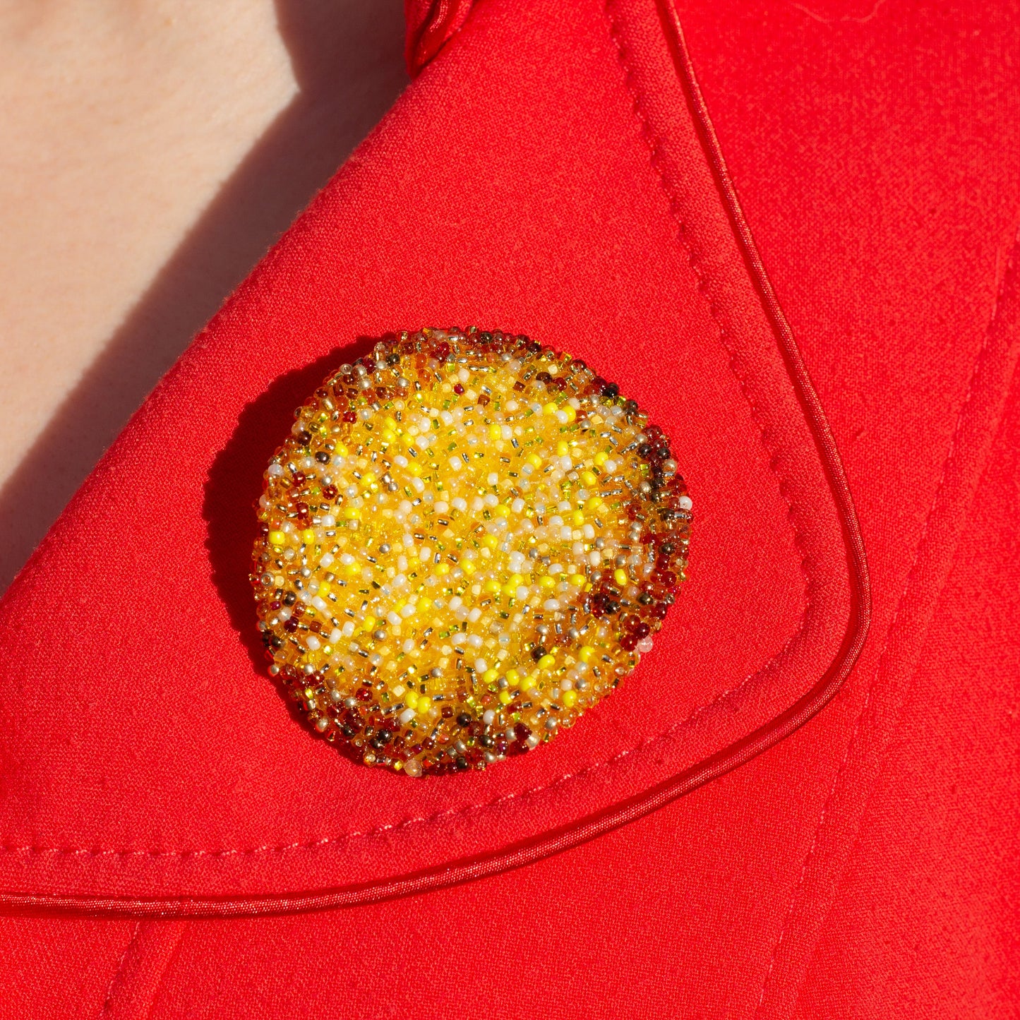 Closeup detail of a yellow handmade beaded potato chip brooch shown on a red coat.