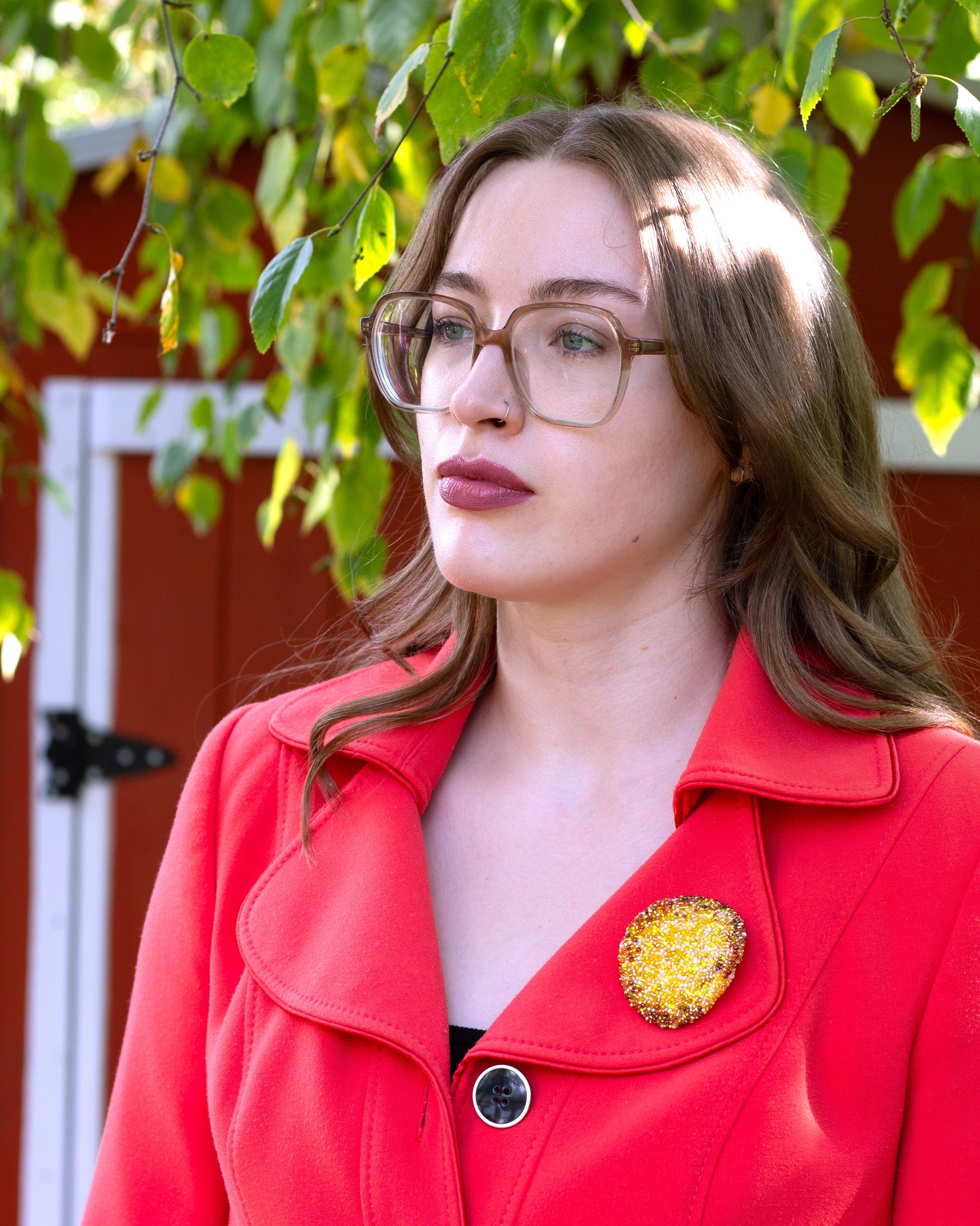 Handmade beaded potato chip brooch worn on a red coat by a young woman set against a red barn door.
