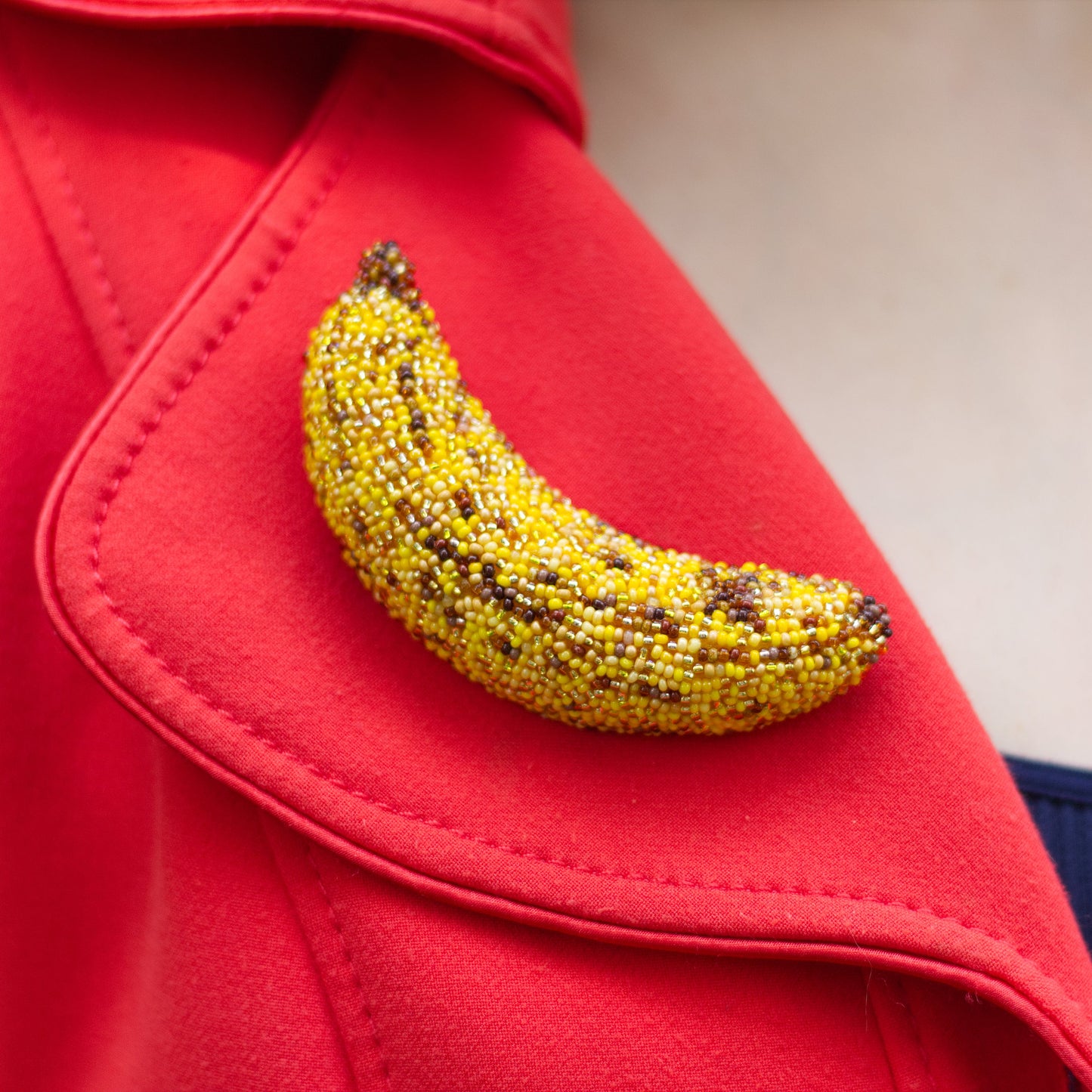 A close-up of a yellow beaded bruised banana brooch pinned onto a bright red coat lapel.