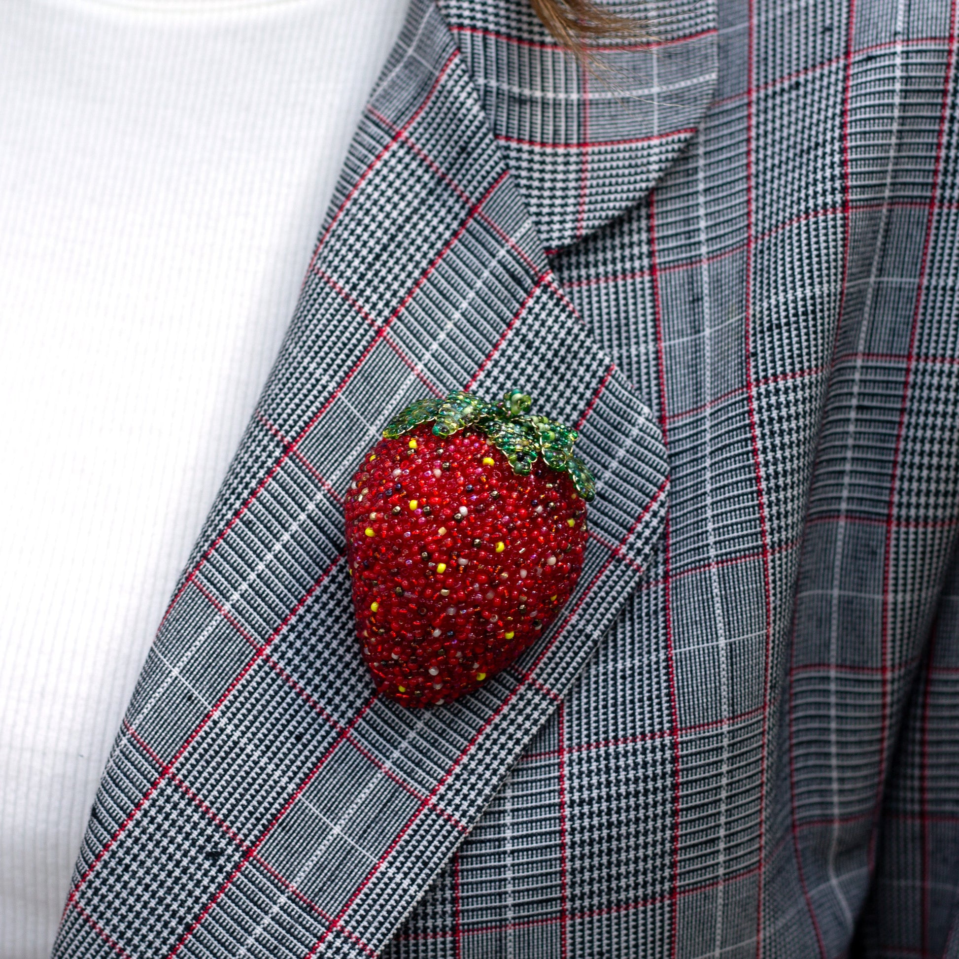 Closeup of a handmade beaded strawberry brooch worn on a plaid jacket lapel.