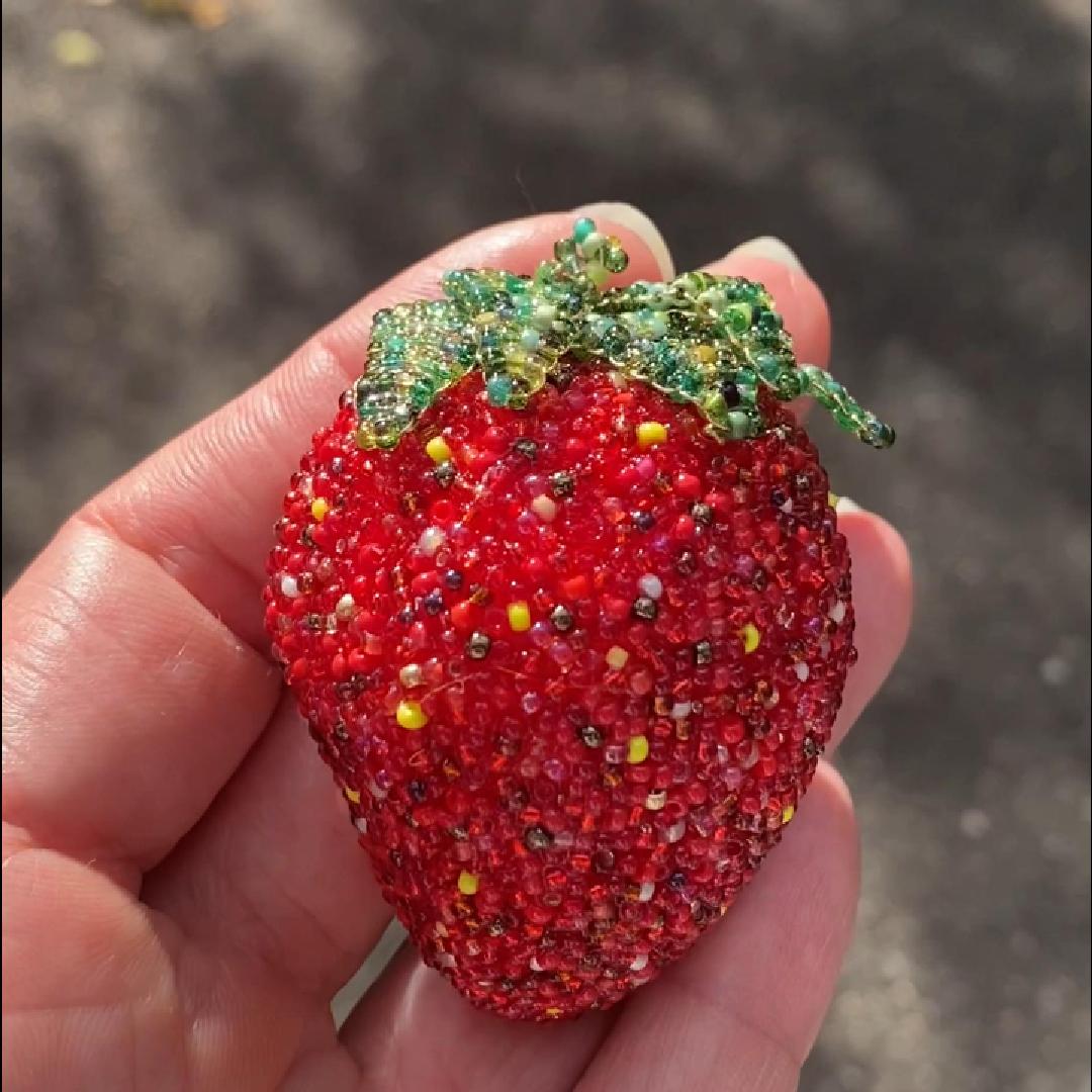 Hand holding a beaded strawberry brooch in the sunlight.
