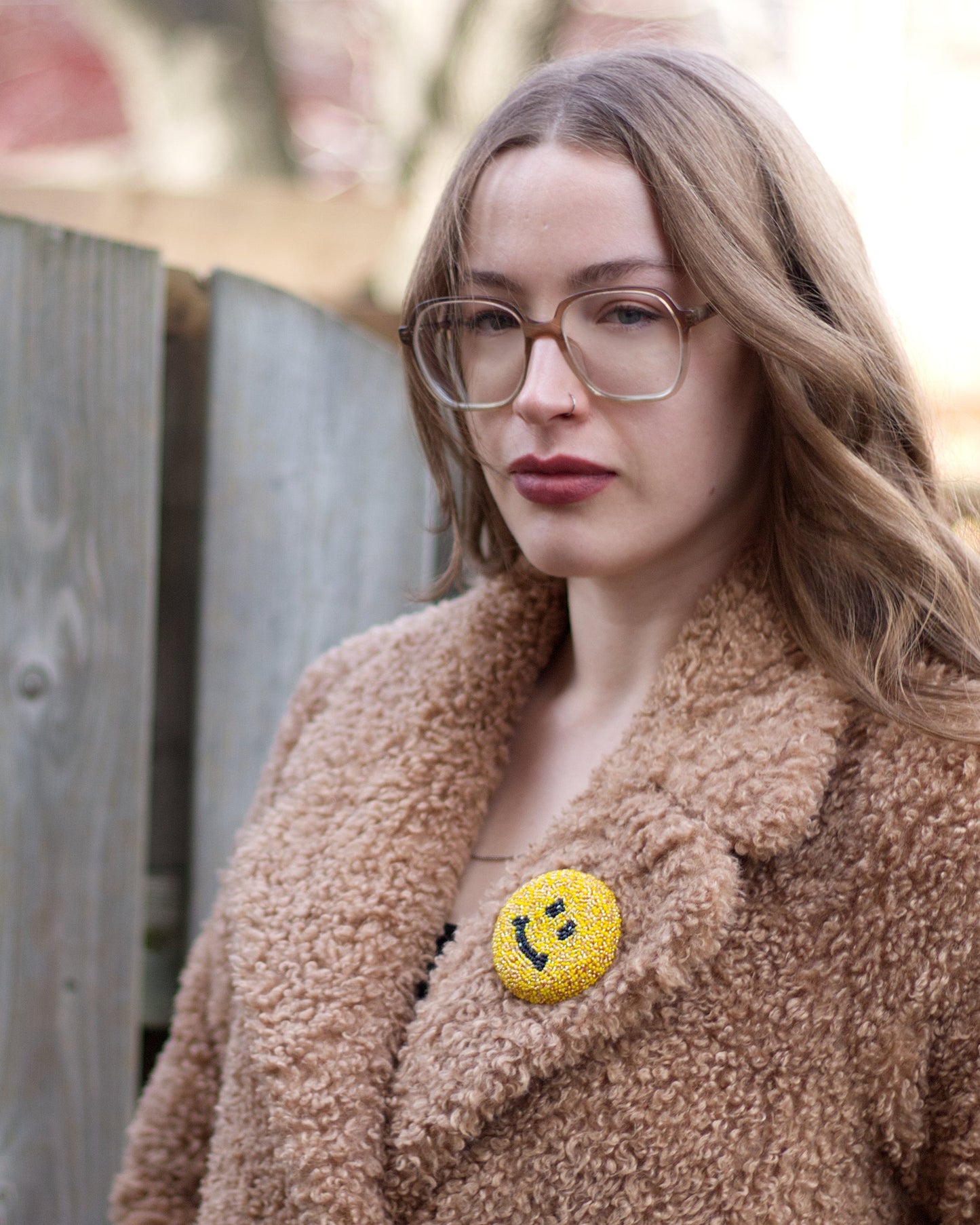 Woman in a brown coat wearing a handmade beaded smiley face brooch.