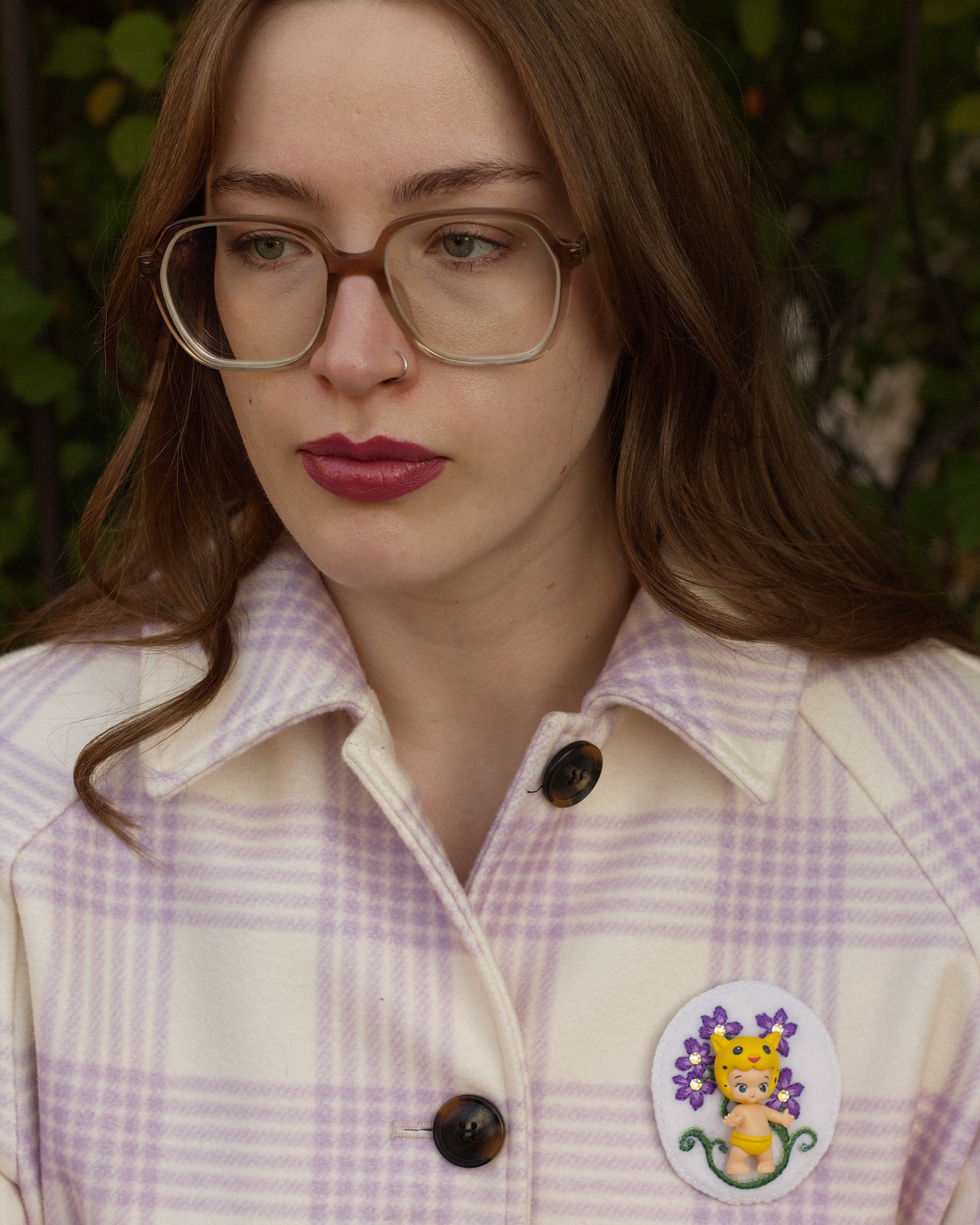 Handmade embroidered floral brooch featuring Lippy Twozie worn on a plaid coat by a young woman.