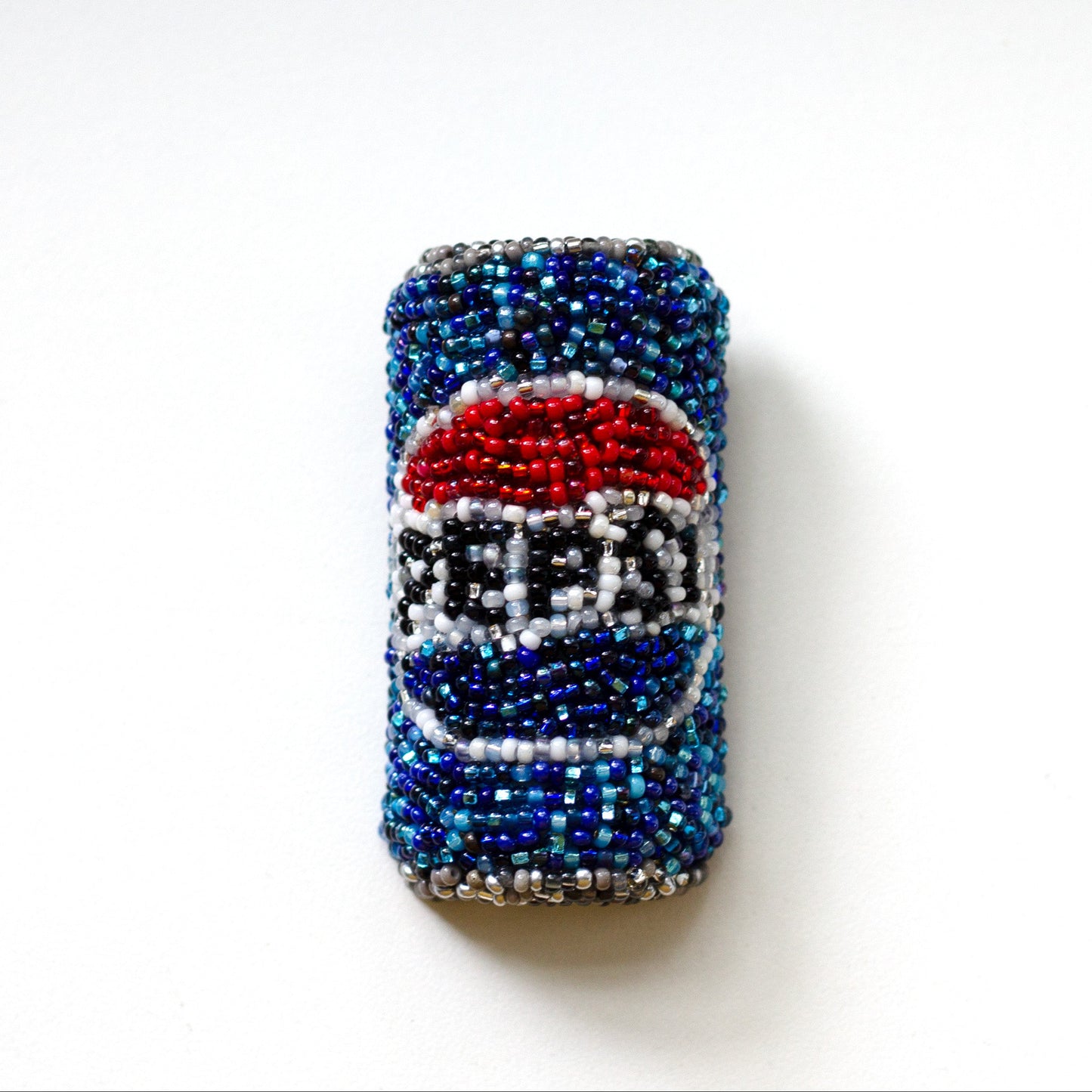 A beaded Pepsi can brooch, featuring blue, red, white, and silver beads, centered on a plain white background.