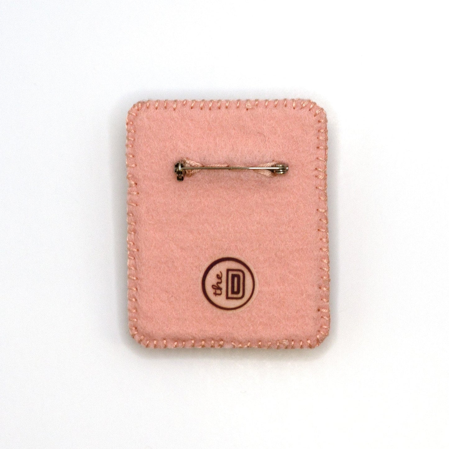 Back view of a handmade embroidered Hello Kitty brooch on a white background showing pin fastener.