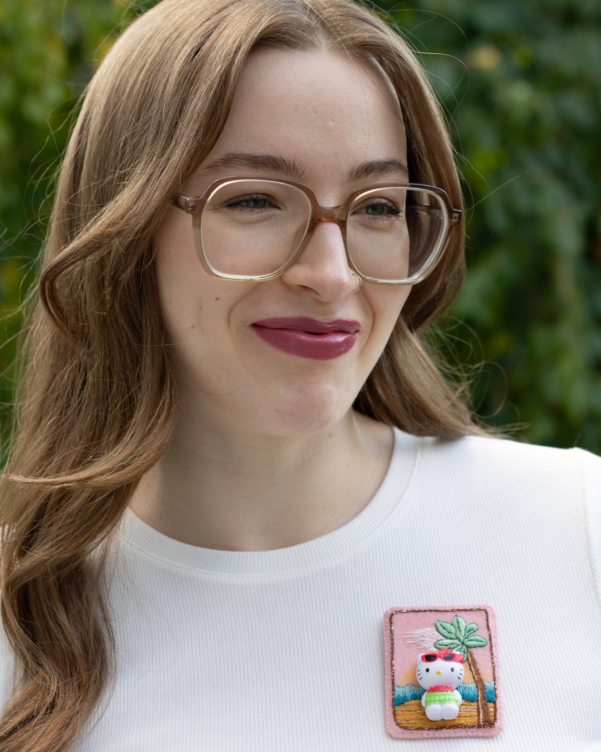 Handmade embroidered Hello Kitty brooch worn on a white t-shirt by a young woman.