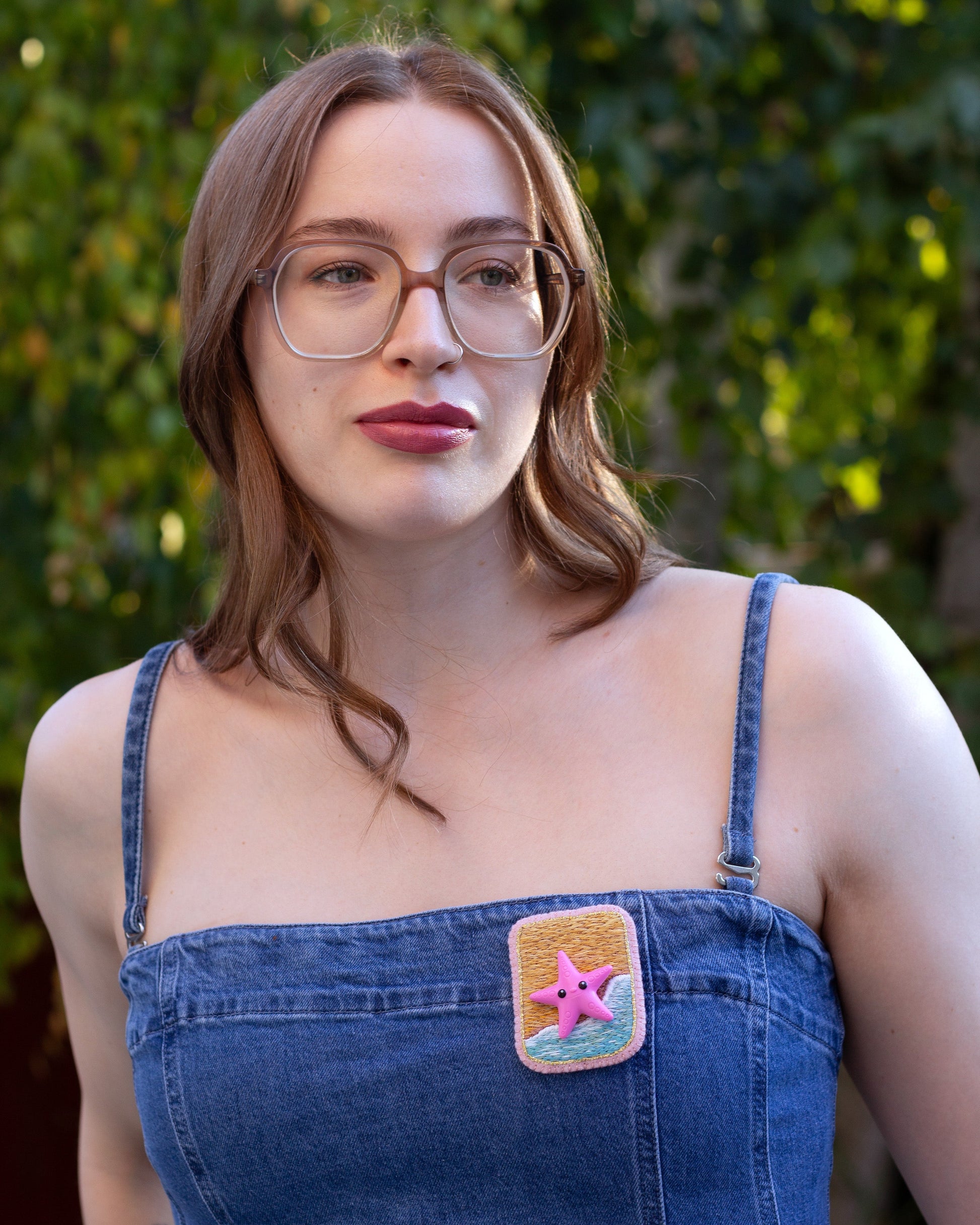 Handmade embroidered beach scene brooch featuring a starfish worn on a denim dress by a young woman.